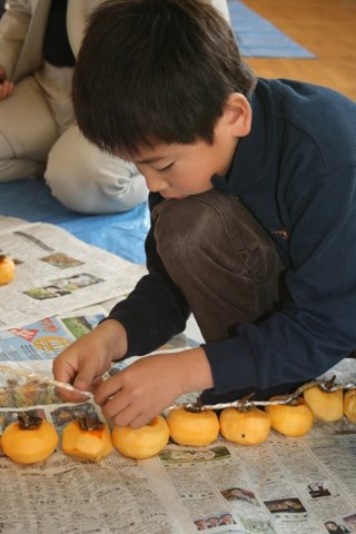 写真：柿を紐に結ぶ寺津小学校児童