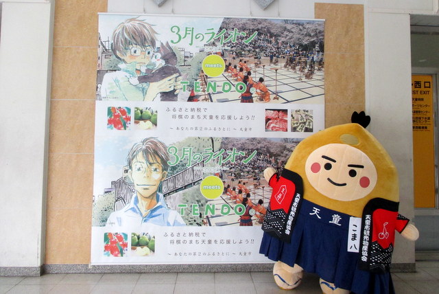 写真：「３月のライオン」と天童市のコラボポスターの前でポーズを決める「天童こま八」（『山形日和。』花回廊キャンペーン」）